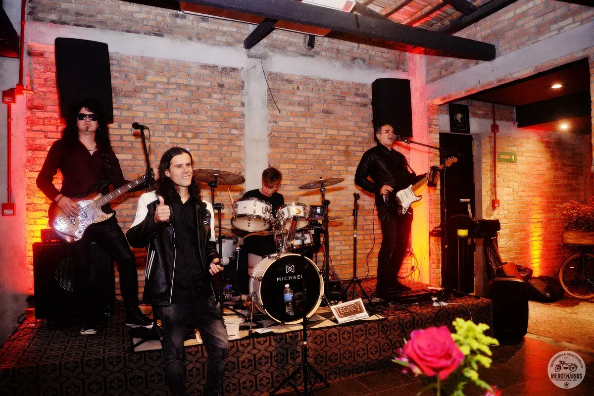 Banda de rock tocando no salão do Mercenários sob luz vermelha
